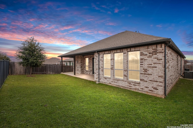 back of property at dusk featuring a patio, brick siding, a lawn, and a fenced backyard