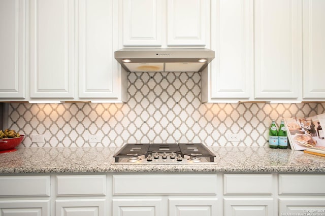 kitchen featuring light stone counters, white cabinets, stainless steel gas stovetop, and extractor fan