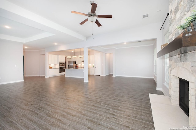 unfurnished living room featuring baseboards, visible vents, a fireplace with raised hearth, ceiling fan, and wood finished floors