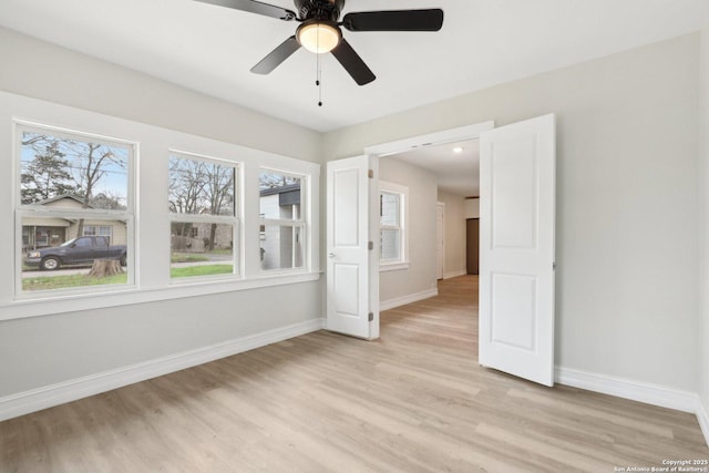 empty room featuring light wood finished floors, a ceiling fan, and baseboards