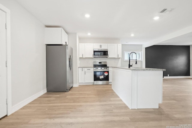 kitchen with baseboards, white cabinets, light stone countertops, stainless steel appliances, and light wood-style floors