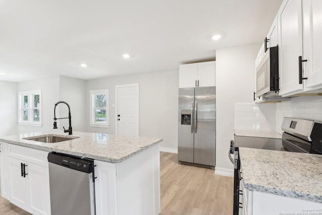 kitchen with light stone counters, a kitchen island with sink, stainless steel appliances, a sink, and white cabinetry