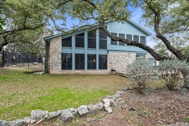 back of house with stone siding, a yard, fence, and a sunroom