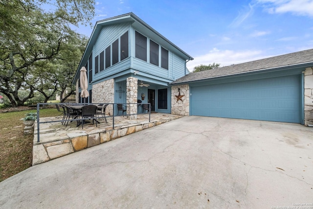 view of front of property featuring an attached garage, stone siding, concrete driveway, and a patio