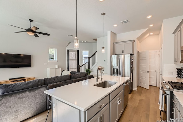 kitchen featuring stainless steel appliances, a sink, open floor plan, light countertops, and an island with sink