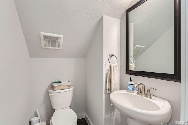 bathroom featuring a textured ceiling, toilet, a sink, visible vents, and baseboards