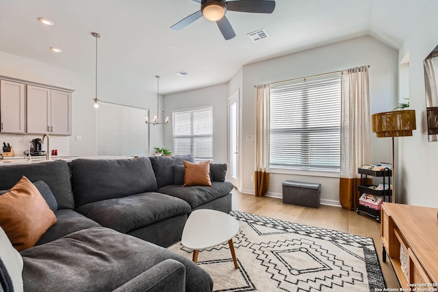 living room featuring light wood-style flooring, visible vents, baseboards, and ceiling fan with notable chandelier