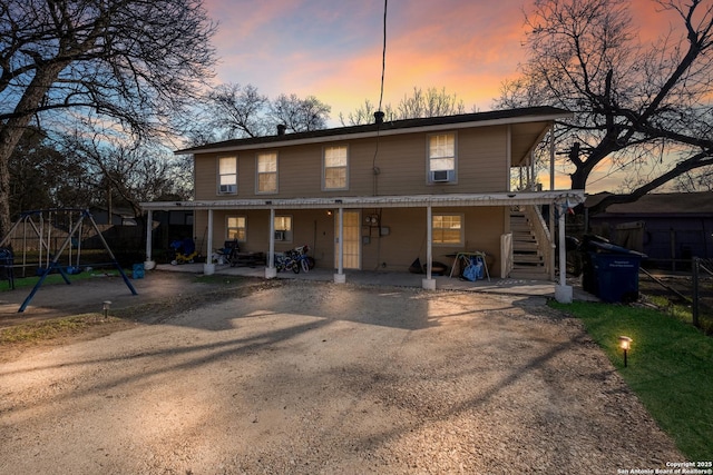 back of house at dusk with a patio area, a playground, and driveway