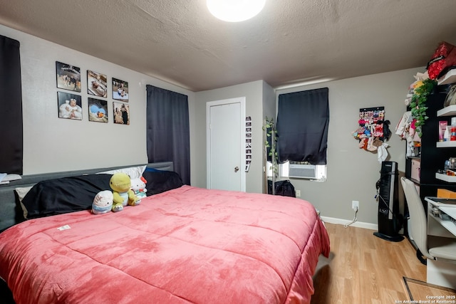 bedroom with cooling unit, baseboards, a textured ceiling, and light wood finished floors