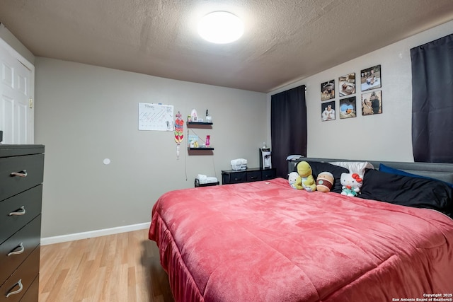 bedroom featuring light wood-style floors, a textured ceiling, and baseboards