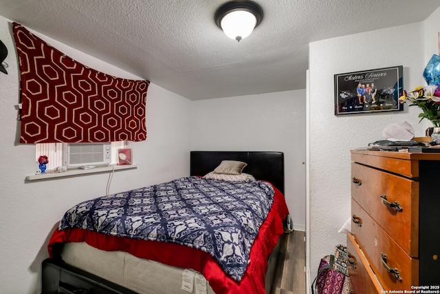 bedroom with cooling unit, a textured wall, a textured ceiling, and wood finished floors