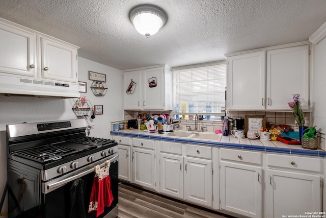 kitchen with stainless steel gas range oven, under cabinet range hood, a sink, white cabinetry, and tile counters