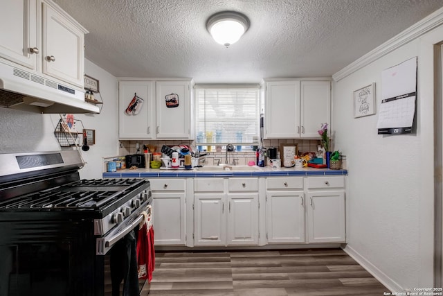 kitchen with light wood finished floors, stainless steel gas range, under cabinet range hood, white cabinetry, and a sink