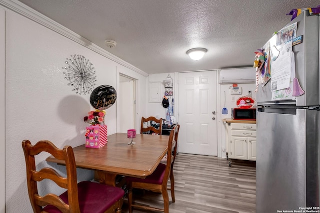 dining area with a textured ceiling, an AC wall unit, crown molding, and light wood-style floors