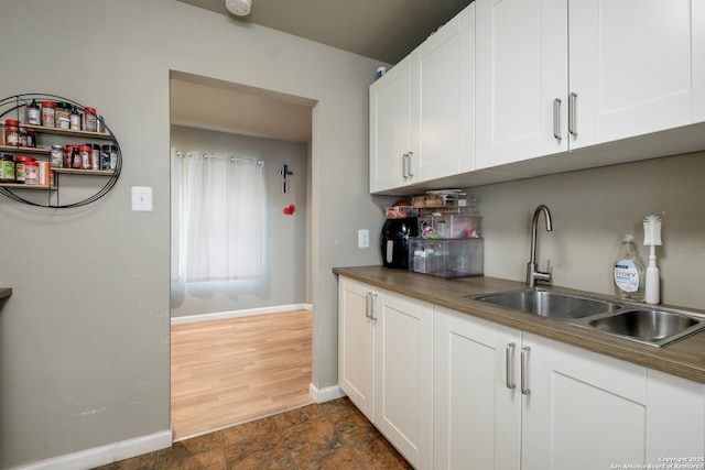 kitchen with a sink, baseboards, white cabinets, wooden counters, and stone finish flooring