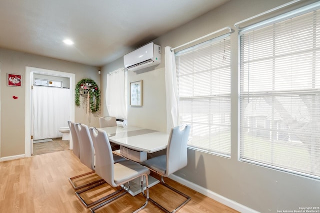 dining area featuring baseboards, a wall unit AC, and light wood-style floors