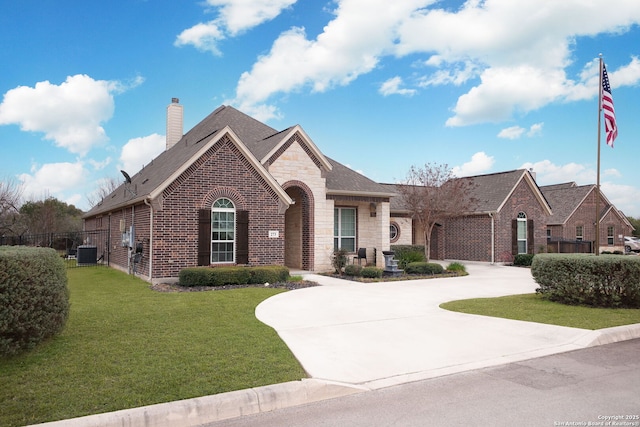 french country style house with brick siding, driveway, a front lawn, and central AC unit