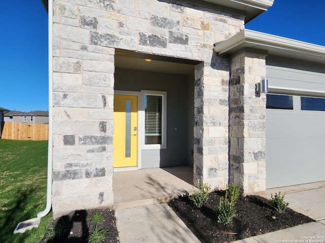 entrance to property with a garage, stone siding, and fence