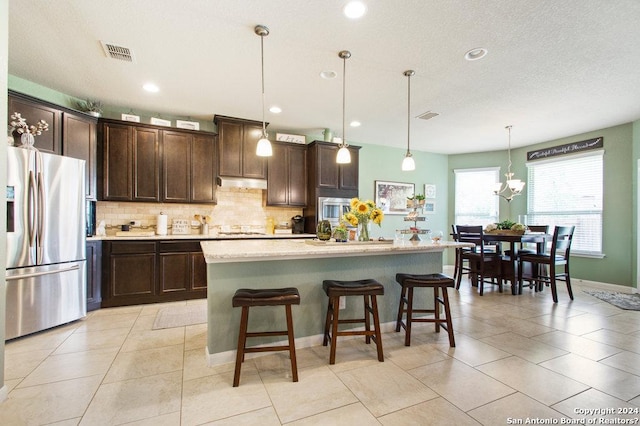 kitchen featuring stainless steel fridge, a center island with sink, a kitchen breakfast bar, hanging light fixtures, and under cabinet range hood