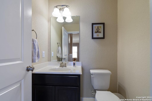 half bathroom featuring a textured wall, vanity, and toilet