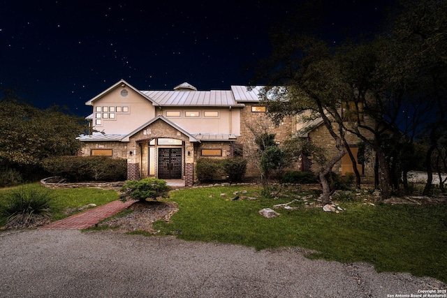 view of front of property featuring a standing seam roof, stone siding, a lawn, and french doors