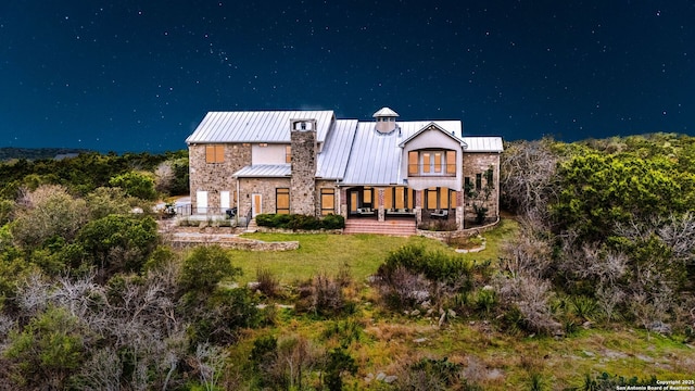 back of house featuring stone siding, metal roof, a standing seam roof, and a lawn