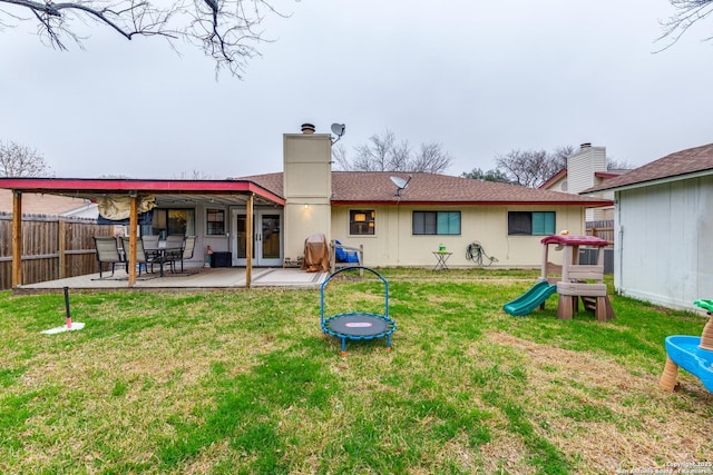 rear view of house featuring a trampoline, a yard, a chimney, a patio, and fence