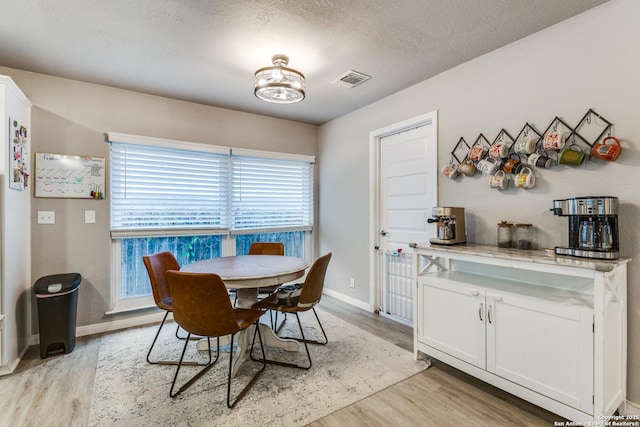 dining room featuring a textured ceiling, visible vents, light wood-style flooring, and baseboards