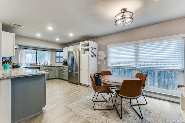 kitchen featuring visible vents, light stone counters, freestanding refrigerator, light wood-type flooring, and a sink