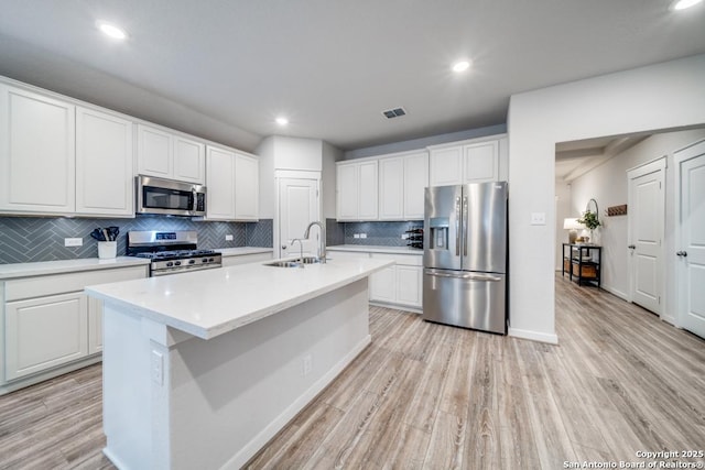 kitchen with stainless steel appliances, an island with sink, light countertops, and white cabinetry