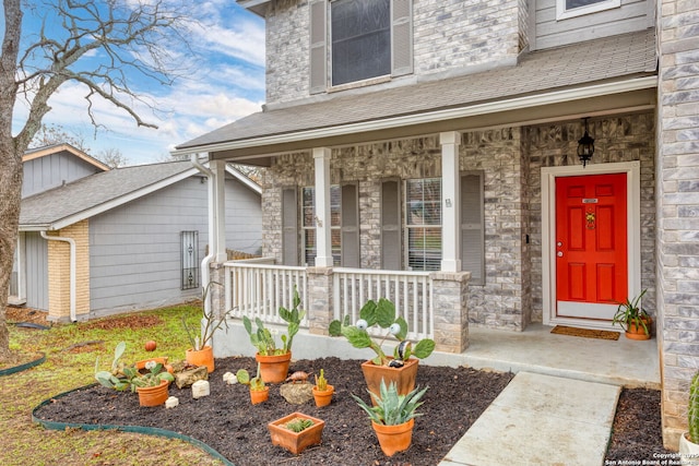 doorway to property featuring covered porch, stone siding, and roof with shingles