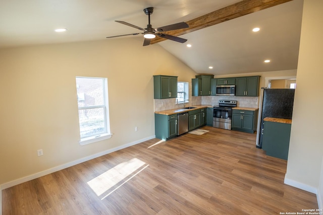 kitchen with stainless steel appliances, a sink, green cabinets, light countertops, and decorative backsplash