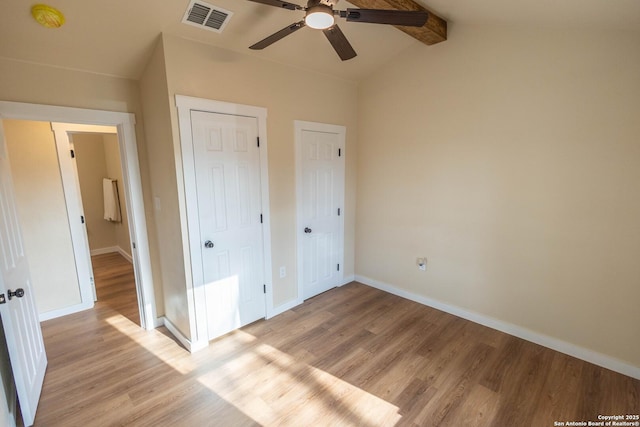 unfurnished bedroom featuring visible vents, baseboards, a ceiling fan, light wood-style flooring, and vaulted ceiling with beams