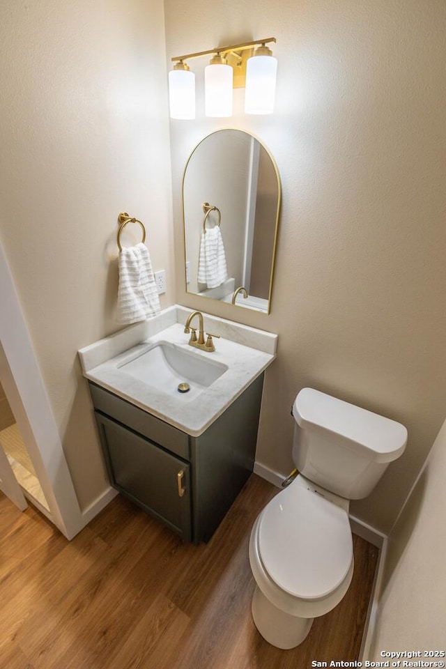 bathroom featuring toilet, baseboards, wood finished floors, and vanity