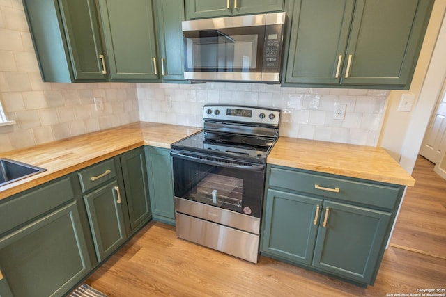 kitchen featuring light wood finished floors, green cabinetry, butcher block countertops, appliances with stainless steel finishes, and backsplash