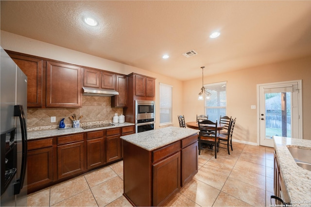 kitchen with tasteful backsplash, visible vents, appliances with stainless steel finishes, hanging light fixtures, and under cabinet range hood