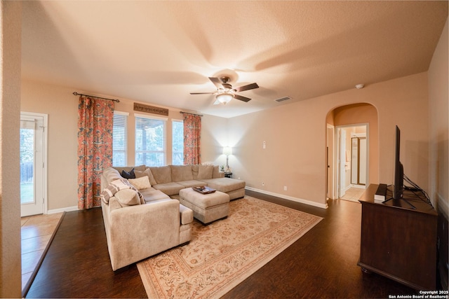 living area with baseboards, visible vents, arched walkways, dark wood finished floors, and a ceiling fan