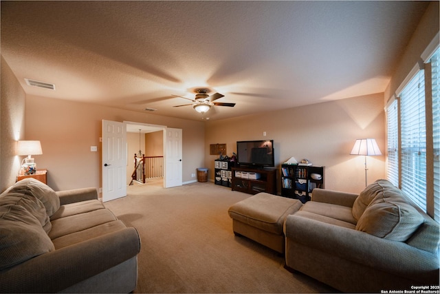 living room featuring a textured ceiling, light colored carpet, a ceiling fan, baseboards, and visible vents