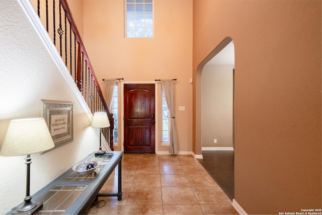 entrance foyer with baseboards, arched walkways, a wealth of natural light, and tile patterned floors