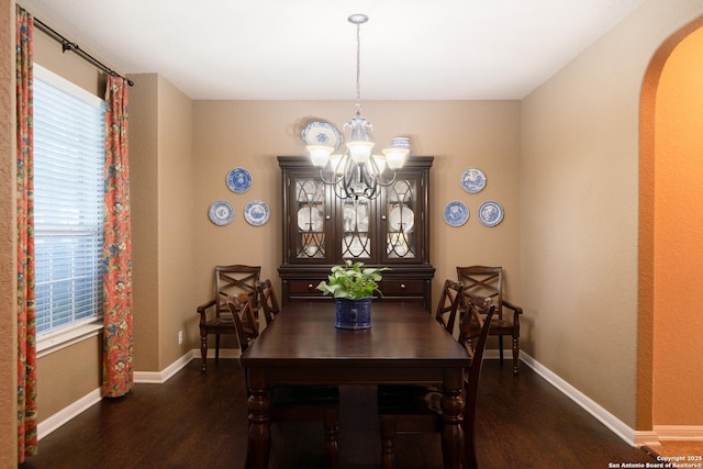 dining area with baseboards, a notable chandelier, arched walkways, and dark wood-type flooring