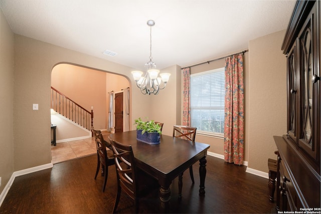 dining space with dark wood-style floors, arched walkways, stairway, a chandelier, and baseboards