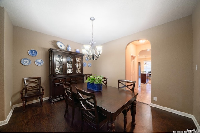 dining room featuring arched walkways, baseboards, dark wood-style floors, and an inviting chandelier