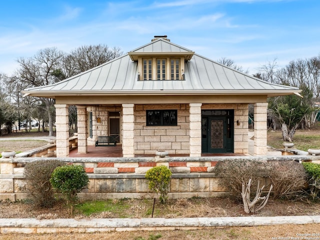 view of front of home featuring metal roof, stone siding, a standing seam roof, and a chimney