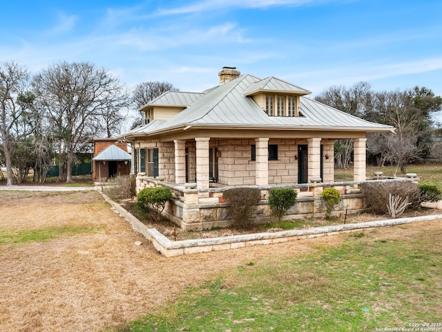 view of front of property with a chimney, a standing seam roof, metal roof, stone siding, and a front lawn