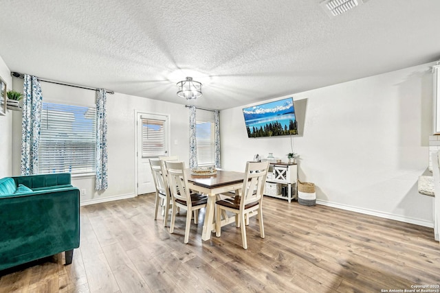 dining room with baseboards, visible vents, wood finished floors, a textured ceiling, and a chandelier