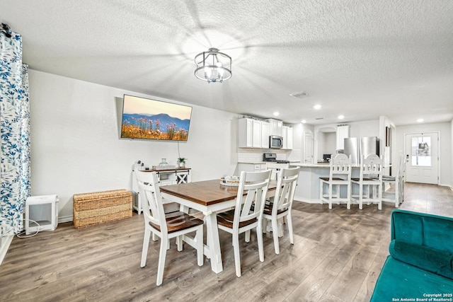 dining space with recessed lighting, a textured ceiling, light wood finished floors, and an inviting chandelier