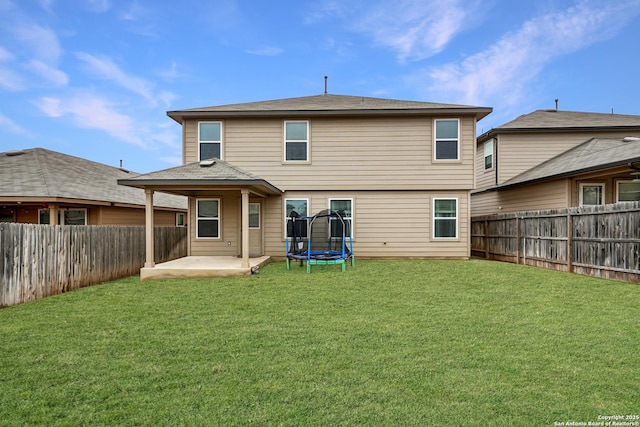 back of property with a trampoline, a yard, a patio, and a fenced backyard