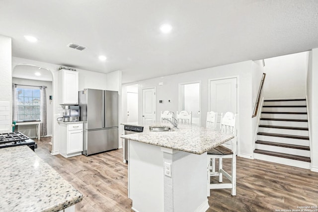 kitchen with stainless steel appliances, visible vents, a kitchen island with sink, white cabinets, and a sink