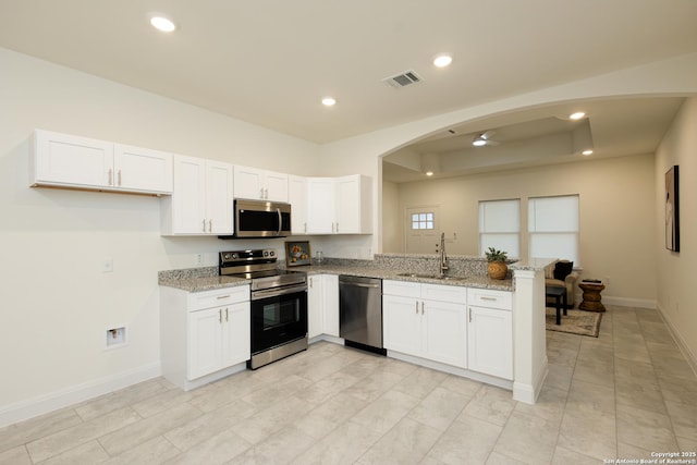 kitchen with stainless steel appliances, visible vents, a sink, light stone countertops, and a peninsula