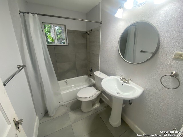 bathroom featuring tile patterned floors, a textured wall, toilet, and shower / bath combo with shower curtain